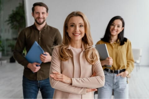 Three professionals in formal attire standing in a well-lit office, engaged in a discussion.
